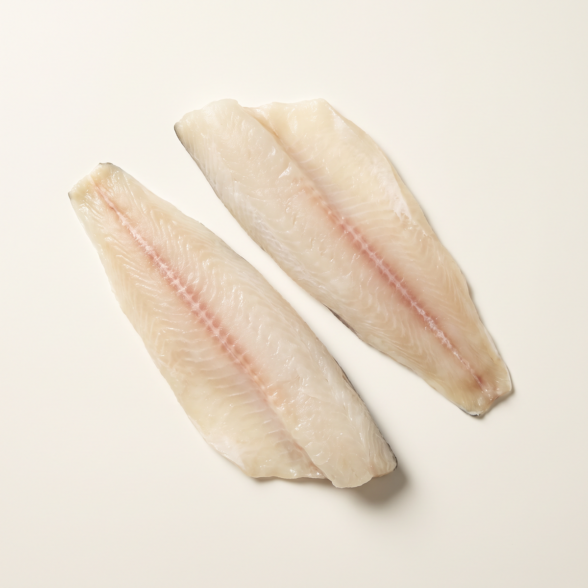 two raw skinless basa catfish fillets, elongated tapered shape, ivory-white flesh with subtle pale pink center line