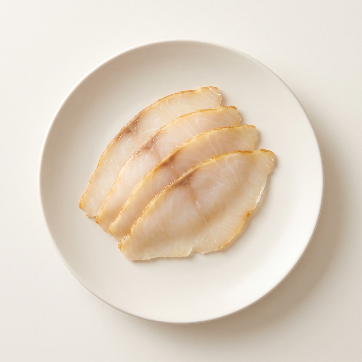 four thin cold-smoked butterfish slices, pale ivory translucent oily flesh, subtle light golden edge, arranged in a small overlapping fan