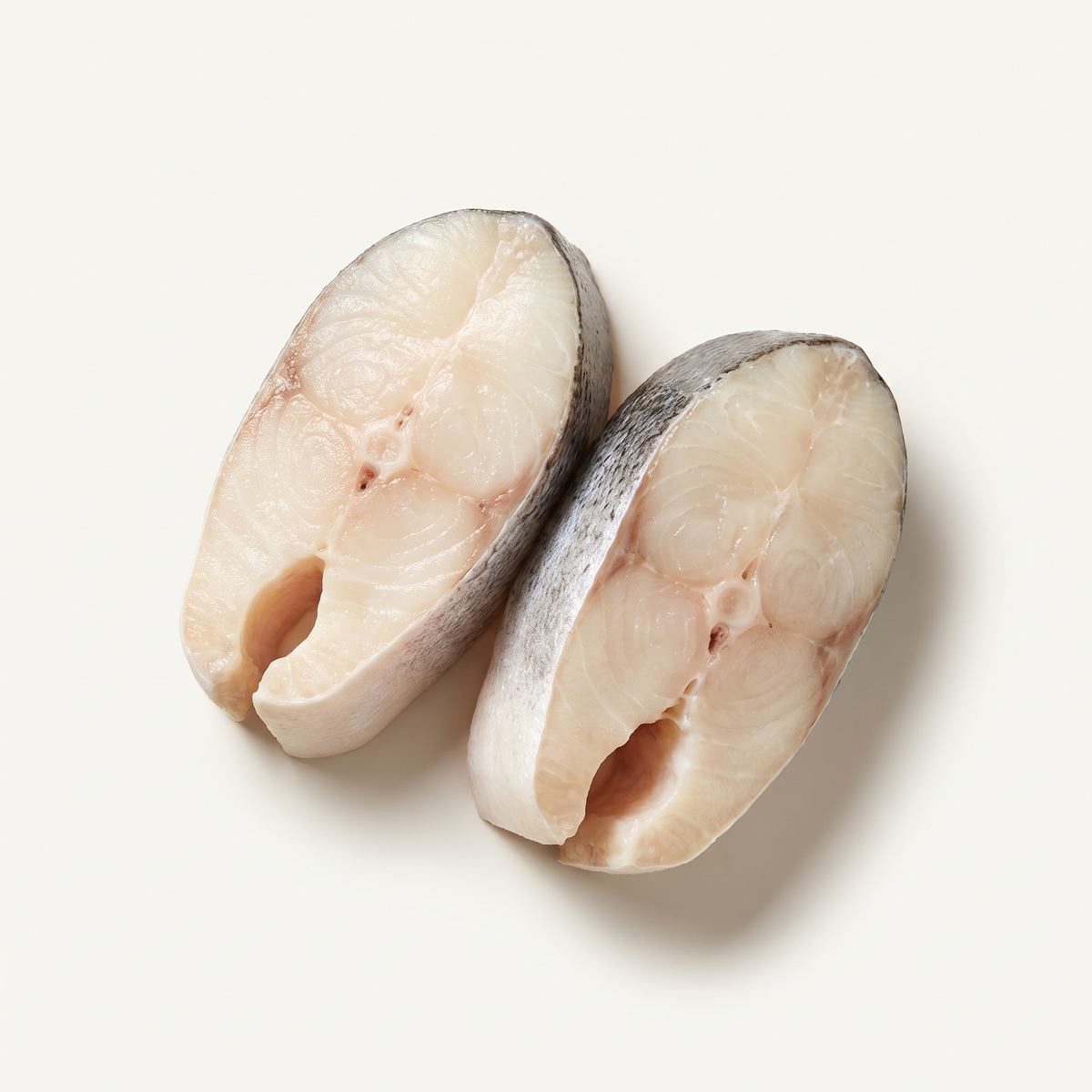 two thick raw Chilean sea bass portions, creamy white firm flesh, silver-grey skin visible on one side, deep rounded cross sections