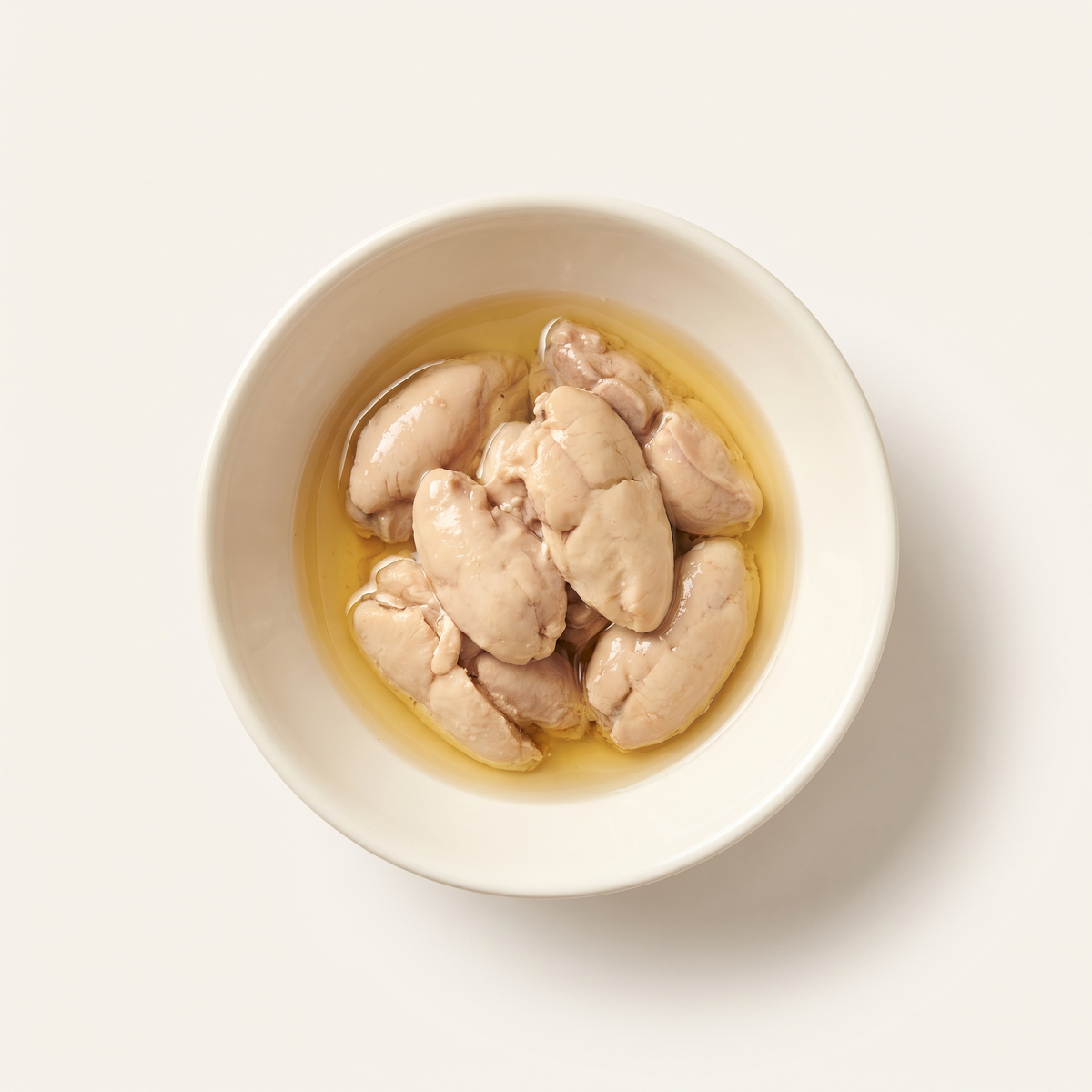 several tender pale beige canned cod liver lobes in a little clear golden oil, served in a shallow plain ivory ceramic bowl, soft delicate lobe texture