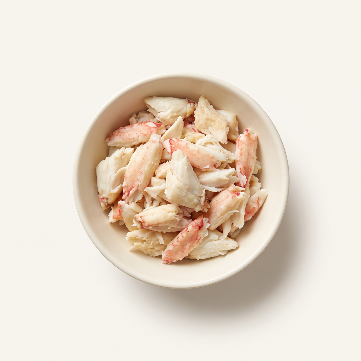 loose cooked picked crab meat in a small plain ivory ceramic bowl, natural white flakes and tender chunks with a few pink-red edges, no imitation sticks