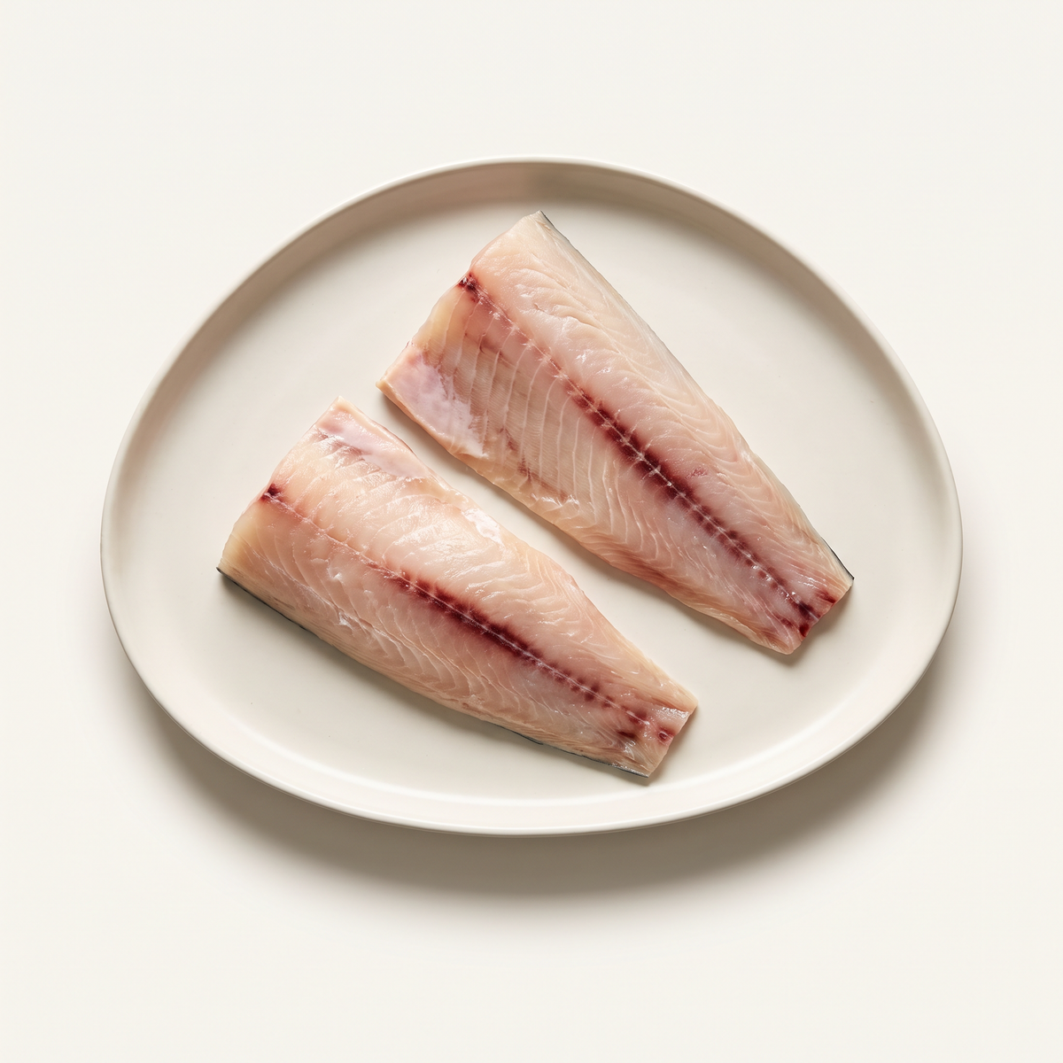 two raw mahi-mahi fillet portions, pale pink-ivory firm flesh and a little dark reddish bloodline, no whole sea bream
